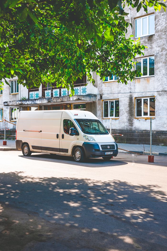 services-02 A white delivery van parked under a tree on a sunny day in an urban area.