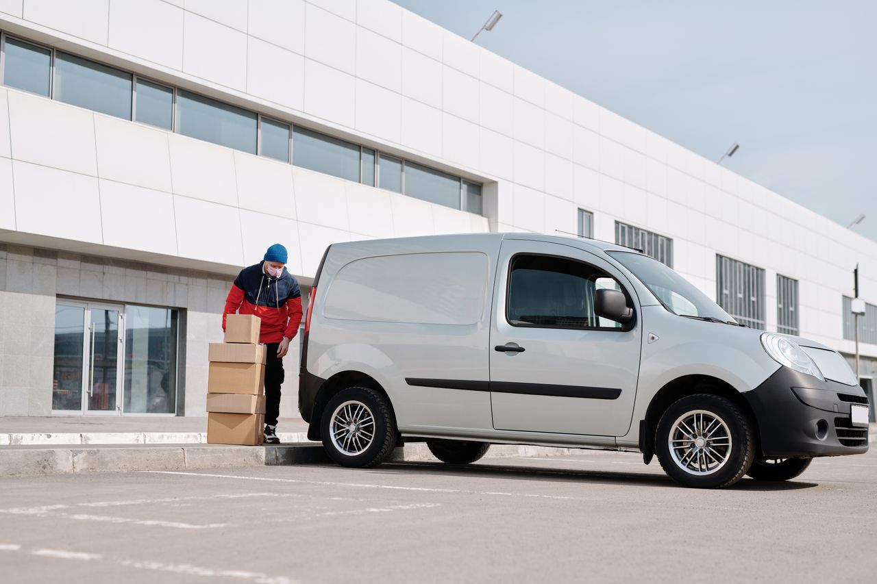services-01 A delivery driver wearing a face mask unloads packages from a van outside a modern building.