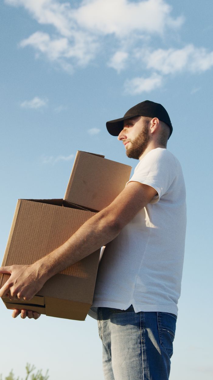 A delivery man carrying boxes outdoors with a blue sky background, symbolizing logistics and efficiency.