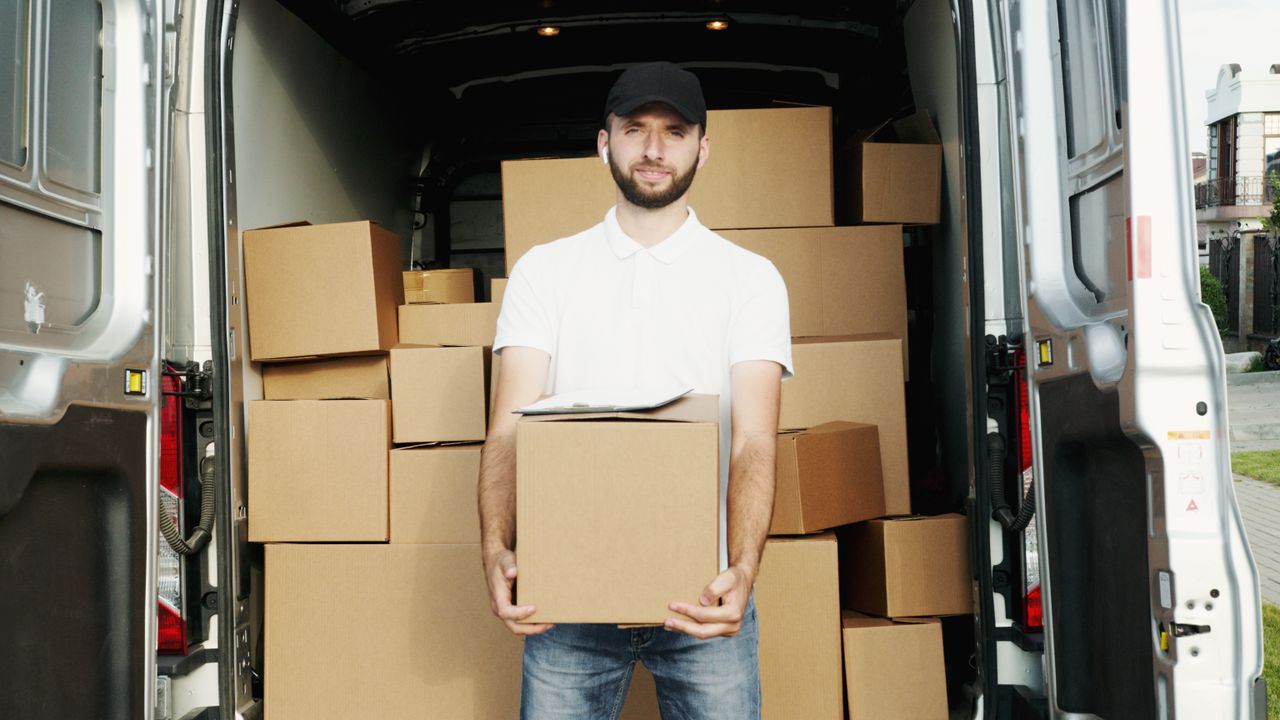 our-stories A courier standing at the back of a van holding a package for delivery.