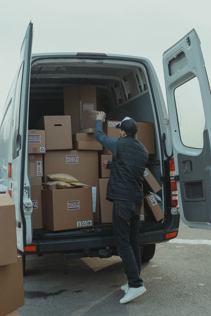 who-we-are A courier organizing boxes in a delivery van for shipment on a cloudy day.