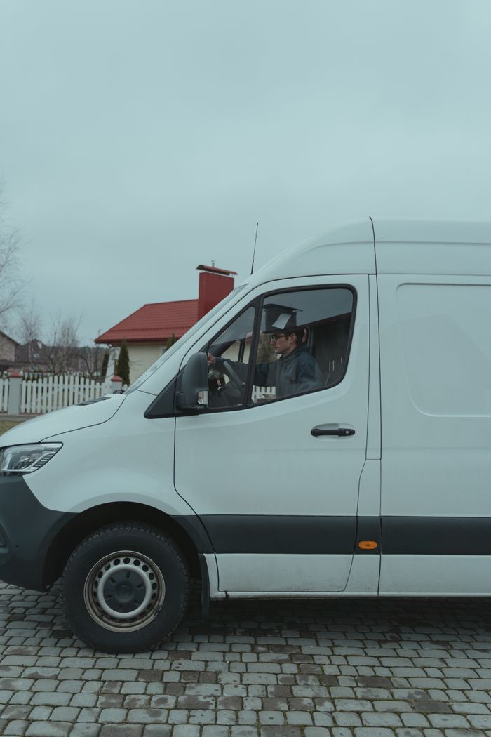 services-03 Driver in a white van parked on a suburban cobblestone street.